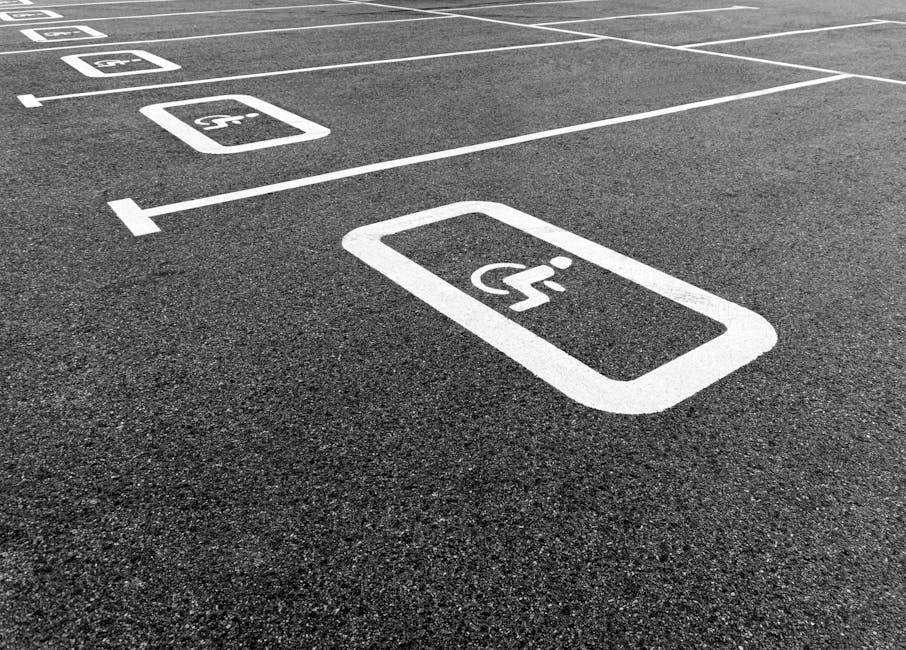 A close-up view of a dark asphalt parking lot surface displaying white painted parking space markings, including a designated handicapped parking spot with a wheelchair symbol inside a rectangular out