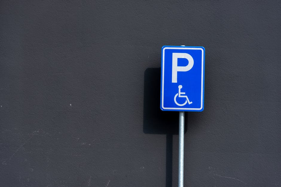 A close-up view of a dark asphalt parking lot surface displaying white painted parking space markings, including a designated handicapped parking spot with a wheelchair symbol inside a rectangular out